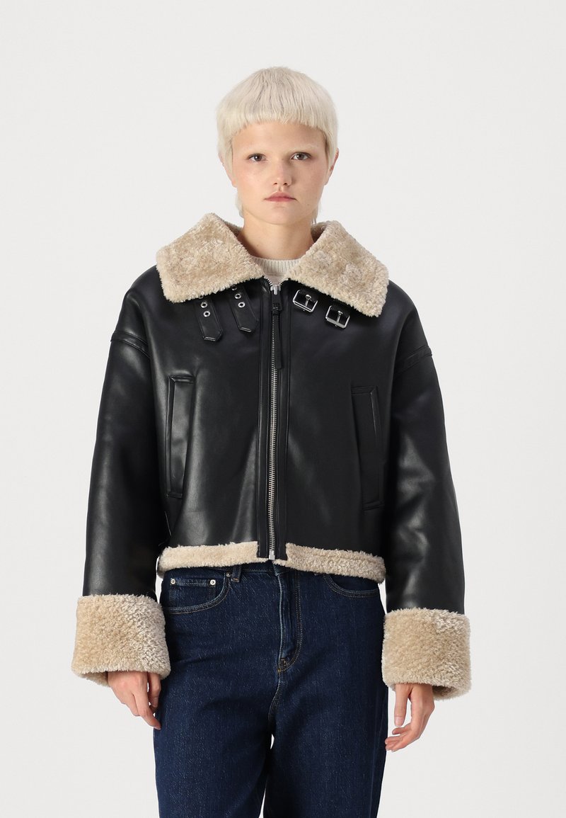 Veste courte en cuir noir avec un col et des poignets en shearling beige, dotée de quincaillerie en argent, d'une fermeture éclair et de poches latérales.