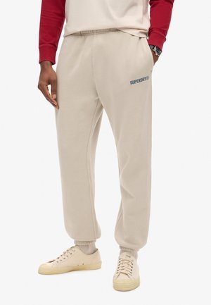 Beige katoenen sweatpants met een taps toelopende pijp, elastische tailleband en geborduurd "Superdry" logo in het blauw. Gestyled met lichtbeige sneakers.