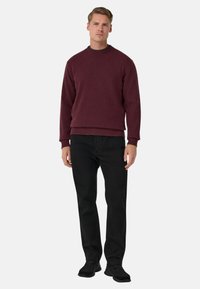 Burgundský pletený svetr s kulatým výstřihem, žebrovanými manžetami a spodním lemem; v kombinaci s černými úzkými kalhotami a černými botami.