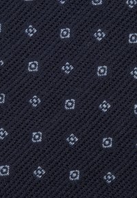 Marineblauer Strickstoff mit einem geometrischen Muster aus kleinen hellblauen und weißen Rauten, der eine strukturierte Oberfläche und eine offene Webart aufweist.