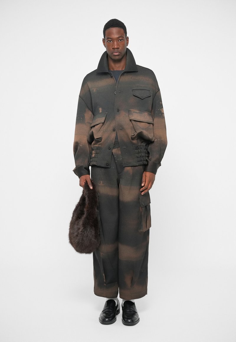 Giacca oversize marrone e nera con tasche a patta e finitura testurizzata, abbinata a pantaloni larghi coordinati e una borsa in pelliccia. Scarpe nere.