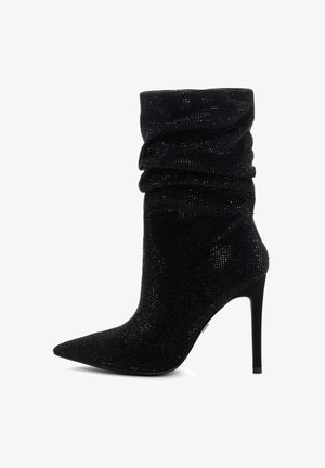 Botín negro hasta el tobillo con una parte superior arrugada, textura con tachuelas, punta afilada y tacón de aguja. Fabricado con un material brillante adornado con strass.