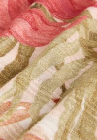 Pehmeä kangas, jossa on kukkakuvio himmeissä vaaleanpunaisen, beigen ja vihreän sävyissä; kangas näyttää yksityiskohtaisen neuletekstuuri ja pehmeät laskokset.