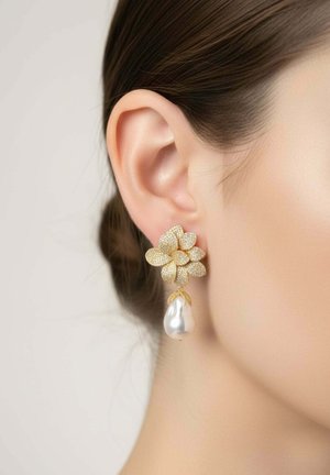 Női fül arany virág alakú fülbevalóval, melynek texturált szirmai és egy nagy, fehér, lógó gyöngycseppje van.