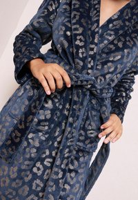 Accappatoio in stampa leopardata blu navy realizzato in tessuto morbido con dettagli metallici. Presenta maniche lunghe, vita con cintura e due tasche laterali.