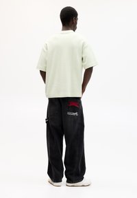 Lysegrøn kortærmet polo-shirt parret med sorte baggy jeans med røde og hvide broderede mønstre på baglommerne. Hvide sneakers.