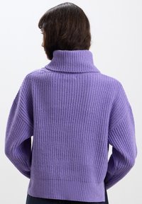 Maglione viola a maglia con colletto alto, caratterizzato da una texture a coste e spalle scese. La vestibilità è rilassata con una lunghezza leggermente accorciata.