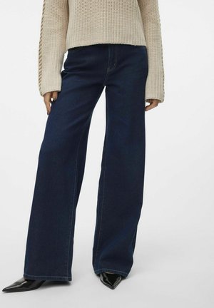 Bredde ben mørk denim jeans med et klassisk femlomme-design og kontrastsying, parret med en strikket cremesværter og spidse sorte hæle.