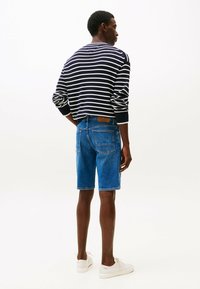 Marineblauwe en witte gestreepte trui met lange mouwen, gecombineerd met blauwe denim shorts en witte sneakers. Eenvoudig ontwerp en relaxte pasvorm.