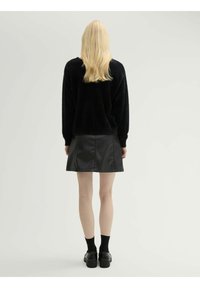 Suéter negro de felpa, falda corta de cuero sintético negro, calcetines hasta el tobillo y zapatos negros. Vista trasera, texturas suaves, diseño sencillo.