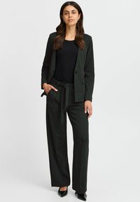 Dámský kostým na míru v černé barvě se vzorem mřížky, který obsahuje fitted blazer a široké kalhoty. Vyrobeno z hladké tkaniny s volným střihem.