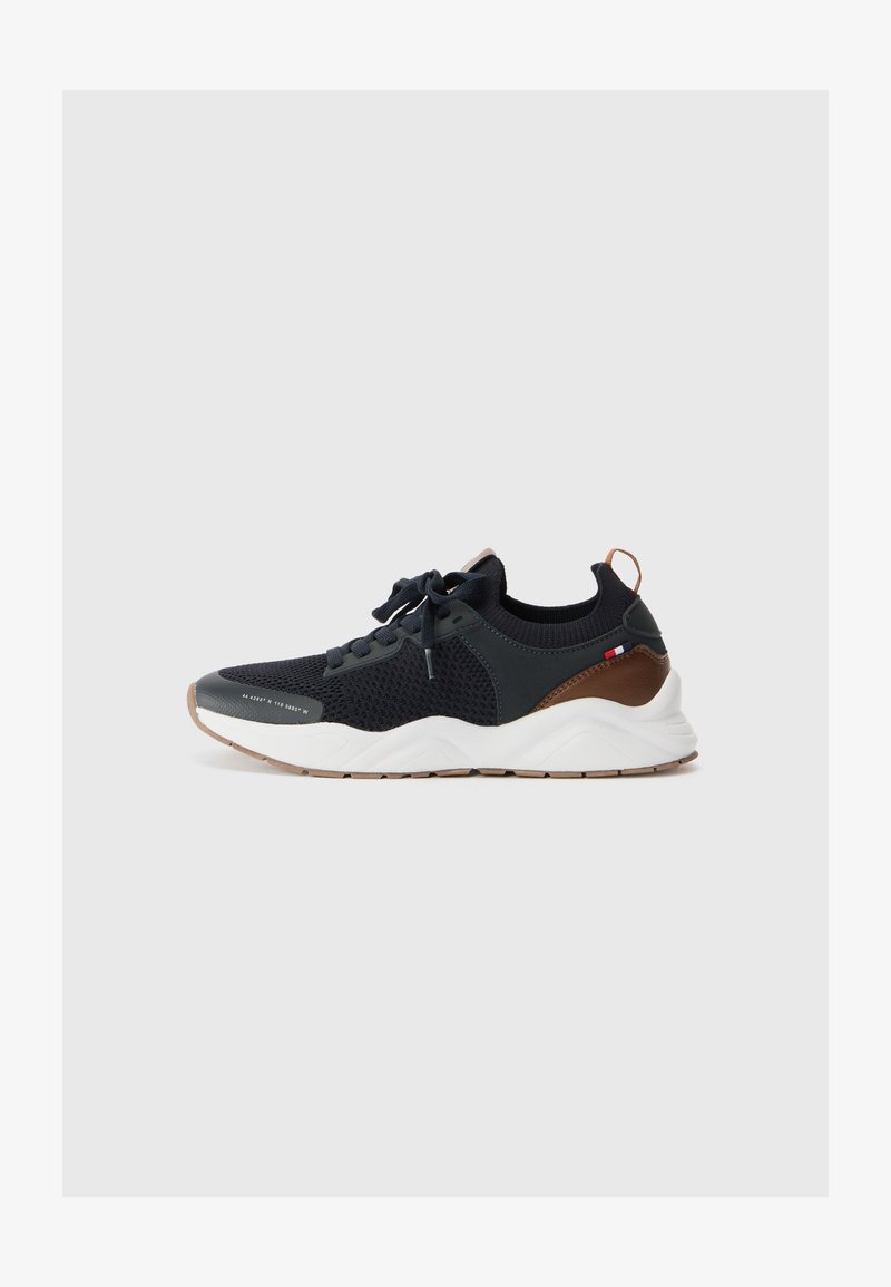 Black athletic sneakers with a textured mesh upper, curved white sole, and brown accents on the heel and sides. Features lace-up design.