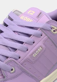 Purple sneaker with textured leather upper, flat lace design, and subtle perforations. Features logo tag and contrasting sole.