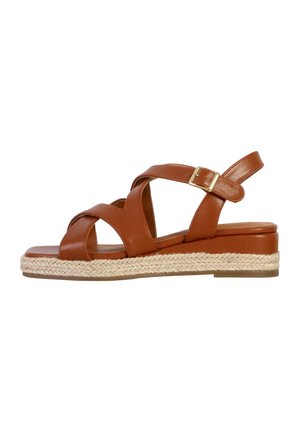 Sandale en cuir marron avec des brides croisées, détail de boucle et plateforme tressée style espadrille. Semelle plate avec une texture minimale.