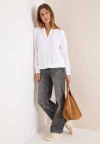 Hvid langærmet bluse med V-udskæring, parret med grå flagrende jeans. Beige sneakers og en lysebrun ruskinds taske fuldender outfittet.
