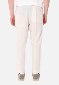 Pantaloni in lino beige chiaro con una vestibilità sartoriale, dotati di una tasca posteriore e di dettagli delle cuciture sottili. Indossati con espadrillas grigie.