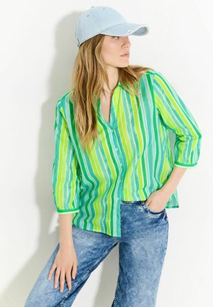 Grön och vit randig knapp-up skjorta i kombination med ljusa denimjeans. Skjortan har en avslappnad passform och 3/4-långa ärmar. En ljusblå keps fulländar stilen.