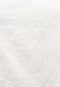 Tissu blanc avec une texture en points en relief répartis uniformément sur la surface, créant un motif subtil.