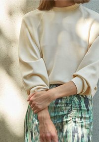 Jersey beige con cuello redondo y mangas largas ligeramente abullonadas, combinado con una falda ajustada de estampado verde con rayas verticales.