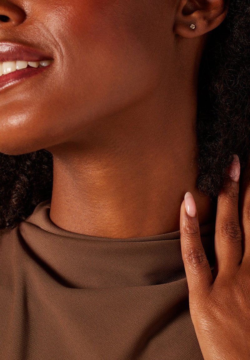 Bruine stoffen top met een hoge halslijn, strak geknipt en toont een gladde huid. Draag oorbellen, korte nude nagels en textuur in het haar zijn zichtbaar.