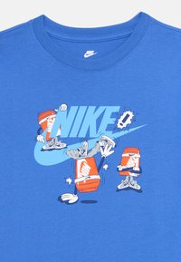Blaues Nike-Shirt mit animierten orangen Wasserflaschen in Sneakers, die um ein großes hellblaues Nike-Logo interagieren.