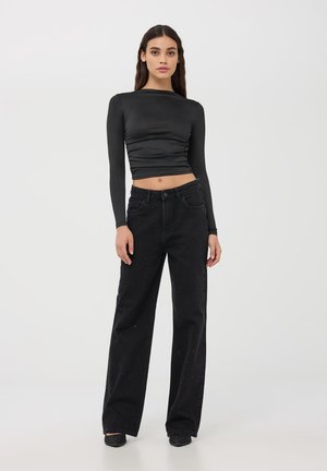 Maglietta nera a maniche lunghe con una silhouette aderente, abbinata a jeans neri a vita alta e larghi con leggere decorazioni e un taglio dritto.