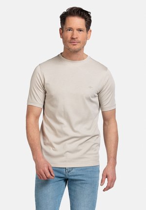 Beige T-shirt met korte mouwen gemaakt van een gladde stof, met een ronde hals en een subtiele logo op de linkerborst. Gepaard met lichtblauwe jeans.