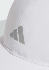 Gorra blanca hecha de tela suave con un sutil logo gris que presenta tres franjas diagonales. Detalles de costura visibles a lo largo del borde.