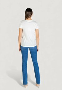 Biała bawełniana koszulka z krótkimi rękawami, okrągłym dekoltem i lekko dopasowanym krojem, zestawiona z niebieskimi dżinsami i beżowymi szpilkami.