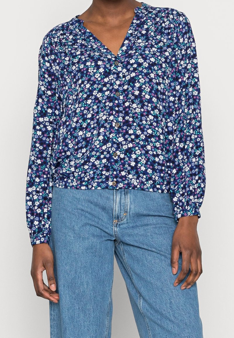 Navyfarbene Bluse mit Blumenmuster und langen Ärmeln, die kleine weiße und rosa Blumen zeigt, mit gerafften Bündchen und einem V-Ausschnitt.
