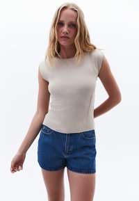 Top smanicato beige a coste con design aderente, abbinato a pantaloni corti in denim blu a vita alta. Look semplice e pulito.