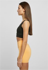 Fekete, vékony pántos crop top sima textúrával, amelyet egy magas derekú, testhezálló, őszibarack színű mini szoknyával viselnek.