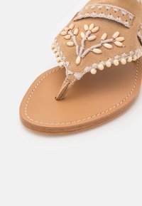 Sandali thong in suede color sabbia con dettagli in perle bianche e foglie ricamate sul cinturino, suola marrone liscia e cuciture decorative.