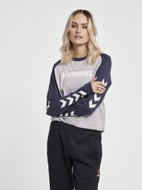 Grå och marinblå skjorta med lång ärm och "HUMMEL"-logotyp; marinblå ärmar har en vit chevronmönster. Svarta sweatpants med sidofickor.