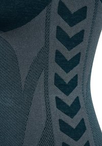 Getextureerde blauw-grijze stof met een visgraatpatroon en gedurfde chevronaccenten aan de zijkant, die verschillende breitechnieken toont.