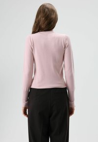 Lichtroze longsleeve met een geribde halslijn, aangesloten in de taille, gecombineerd met zwarte, hoge taillebroek, van achteren weergegeven.