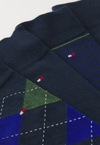 Navy socks featuring geometric patterns: one with green and blue diamonds, the other with blue stripes and small logo accents.