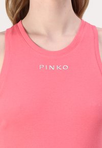 Tetts rosa ribbet tanktopp med rund hals og sølvfarget merke med teksten "PINKO" i midten. Myk tekstur og tettsittende design.