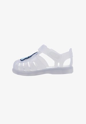 Sandalia de plástico blanca translúcida con diseño abierto, correa ajustable y acento azul en la parte delantera. Textura suave y flexible, adecuada para el uso veraniego.
