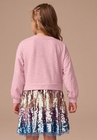 Rózsaszín, texturált hosszú ujjú pulóver, aranyból kékbe áttűnő flitteres szoknyával párosítva. A szoknya fodros kialakítású.