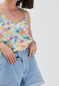 Débardeur à fleurs bleu, jaune et rose avec bretelles spaghetti, associé à un short en jean bleu clair taille haute avec ceinture.
