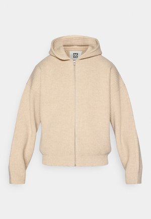 Sweater com capuz bege, de fecho éclair, feito de tecido canelado. Apresenta um fecho à frente e ombros ligeiramente caídos para um ajuste descontraído.