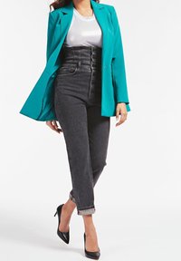 Blazer turquoise sur une chemise blanche, assorti avec un jean noir taille haute à fermeture à boutons et aux poignets retroussés, complété par des talons noirs.