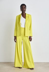 Yellow tailored suit with a structured blazer and wide-leg trousers, paired with a white top. Smooth fabric and minimalistic design.