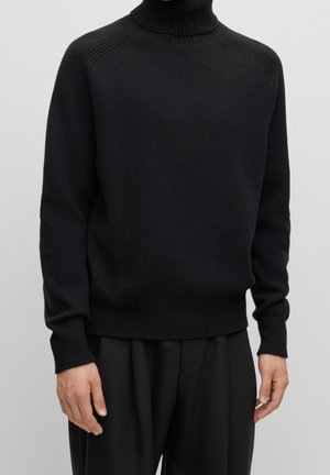 Pull noir à col roulé en tissu tricoté texturé, doté de poignets et d'ourlet côtelés, avec une coupe décontractée et des épaules sans couture.