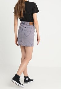 Mini-jupe en jean gris clair avec un ourlet effiloché, dotée de poches arrière et d'une étiquette en cuir marron à la ceinture. Associée à des baskets montantes noires.