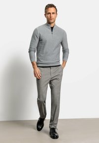 Maglione grigio chiaro con zip e texture a coste, abbinato a pantaloni grigi su misura e scarpe in pelle nere.