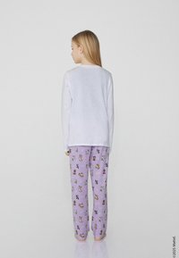 Bílé tričko s dlouhým rukávem a levandulové pyžamové kalhoty s hravým zvířecím vzorem, hladká textilie a volný střih.