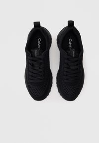 Sapatos atleticos pretos com parte superior em malha, bico redondo, atacadores e sola de borracha. Apresentam um logotipo na lingueta e na aba de calcanhar.