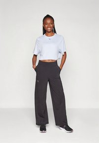 Lichtblauw cropped shirt en zwarte broek met wijde pijpen en zakken, beide met een Puma-logo. Model draagt zwarte sportschoenen.